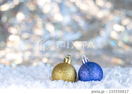 Two glittery Christmas ornaments sit in snow with twinkling lights in a festive winter scene Two glittery Christmas ornaments sit in snow with twinkling lights in a festive winter scene 133550817