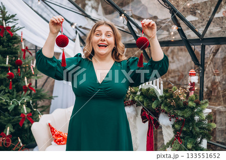Young woman in green dress decorating Christmas tree at home and smiling. Winter time and holidays. Celebration banner Young woman in green dress decorating Christmas tree at home and smiling. Winter time and holidays. Celebration banner 133551652