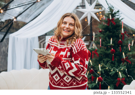 Smiling woman looking at digital tablet and standing near decorated Christmas tree. Winter time and holidays. Celebration banner, big sale concept 133552341