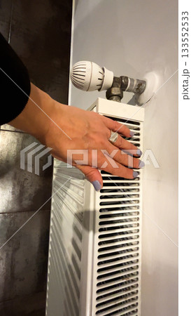 A woman's hand touches the heating battery in the room and determines if it is warm. A woman's hand touches the heating battery in the room and determines if it is warm. 133552533