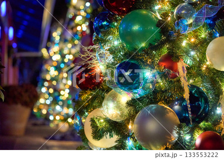 A decorated evergreen is covered with bright baubles, ribbons, and glowing lights. The colorful ornaments sparkle with rich bokeh in the night. A decorated evergreen is covered with bright baubles, ribbons, and glowing lights. The colorful ornaments sparkle with rich bokeh in the night. 133553222