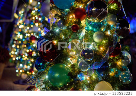 A close view shows shiny red, blue, green, silver, and gold baubles on a lit tree. Soft night bokeh creates a festive, sparkling holiday mood. A close view shows shiny red, blue, green, silver, and gold baubles on a lit tree. Soft night bokeh creates a festive, sparkling holiday mood. 133553223