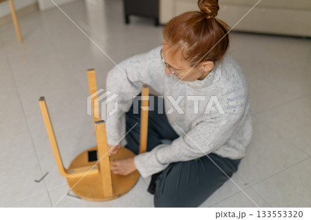 Woman assembling wooden stool with hex wrench at home 133553320