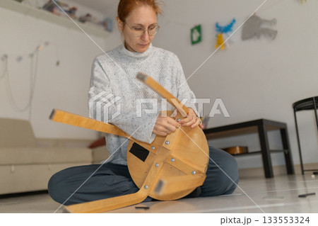 Woman assembling new furniture at home sitting on floor 133553324