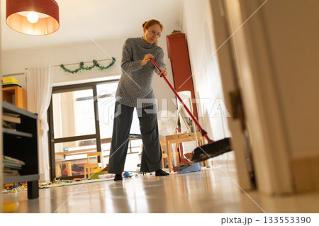 Woman sweeping messy floor in living room Woman sweeping messy floor in living room 133553390