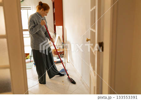 Woman using a broom to clean the floor inside her home Woman using a broom to clean the floor inside her home 133553391