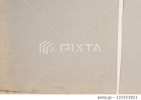 A beige fabric surface shows subtle woven texture with a vertical ribbon-like strip on the right side. Canvas texture, fabric surface close-up, natural simplicity 133553921