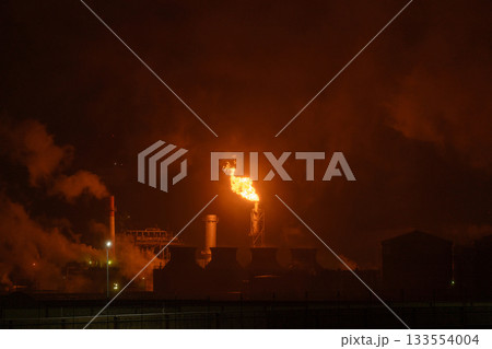 An industrial flare stack burns off excess gas with a large, bright orange flame and thick smoke 133554004