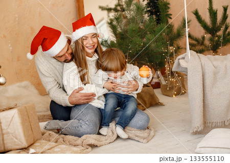 Daddy and mom with their son near christmas tree with lights and gifts hugging and having fun. Cheerful family celebrating Christmas. Mother, father and little boy wearing white sweaters. Daddy and mom with their son near christmas tree with lights and gifts hugging and having fun. Cheerful family celebrating Christmas. Mother, father and little boy wearing white sweaters. 133555110
