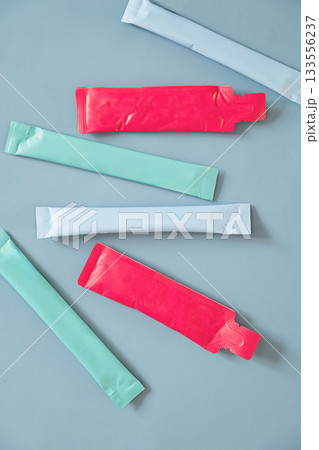 Colorful sachets and stick packs arranged on plain blue background. 133556237