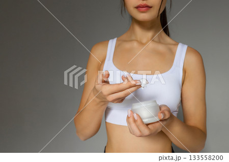 Close-up of a woman applying moisturizing cream to her arm, demonstrating a nourishing skincare step with a jar of body lotion on a neutral background. Close-up of a woman applying moisturizing cream to her arm, demonstrating a nourishing skincare step with a jar of body lotion on a neutral background. 133558200