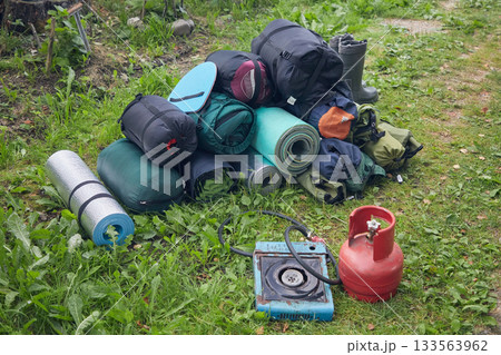 Camping gear piled up near the car: sleeping bags, tents, mats, gas stove Camping gear piled up near the car: sleeping bags, tents, mats, gas stove 133563962