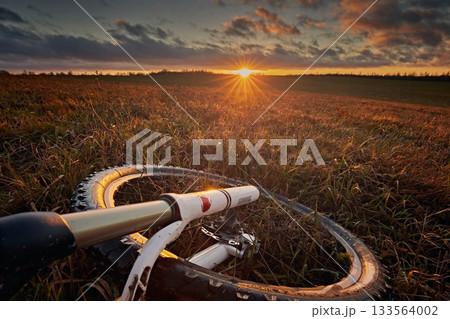 A bicycle wheel against the background of a meadow and a bright sunset sky with the sun. Travel and adventure A bicycle wheel against the background of a meadow and a bright sunset sky with the sun. Travel and adventure 133564002