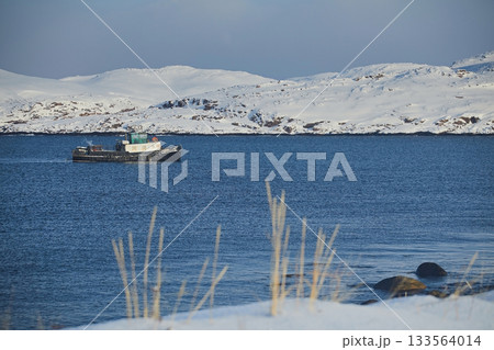 Winter landscape: a ship in the frozen Barents Sea against the background of snow hills and blue sky during the day 133564014