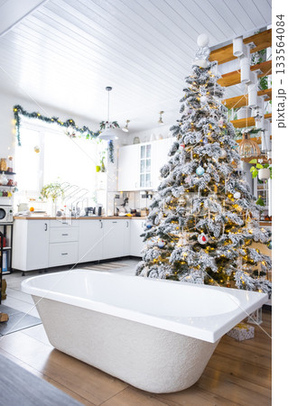 New bathtub under festive Christmas tree as New Year's gift in interior of white modern decorated kitchen. Interior renovation and design, construction and home improvement New bathtub under festive Christmas tree as New Year's gift in interior of white modern decorated kitchen. Interior renovation and design, construction and home improvement 133564084