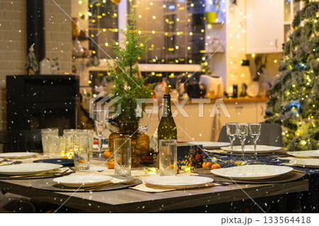 Festive interior of house is decorated for Christmas and New Year in loft style with black stove, fireplace, Christmas tree. Warm studio room with set table, burning wood, cozy and heating of home Festive interior of house is decorated for Christmas and New Year in loft style with black stove, fireplace, Christmas tree. Warm studio room with set table, burning wood, cozy and heating of home 133564418