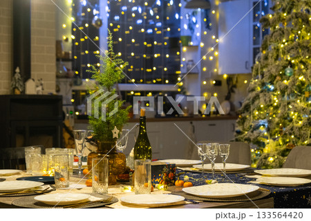 Festive interior of house is decorated for Christmas and New Year in loft style with black stove, fireplace, Christmas tree. Warm studio room with set table, burning wood, cozy and heating of home Festive interior of house is decorated for Christmas and New Year in loft style with black stove, fireplace, Christmas tree. Warm studio room with set table, burning wood, cozy and heating of home 133564420