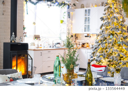 Festive interior of house is decorated for Christmas and New Year in loft style with black stove, fireplace, Christmas tree. Warm studio room with set table, burning wood, cozy and heating of home Festive interior of house is decorated for Christmas and New Year in loft style with black stove, fireplace, Christmas tree. Warm studio room with set table, burning wood, cozy and heating of home 133564449