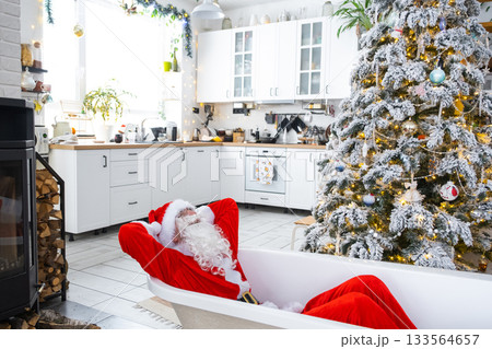 Santa is lying resting in New bathtub under festive Christmas tree as New Year's gift in interior of white modern decorated kitchen. Interior renovation and design, construction and home improvement 133564657