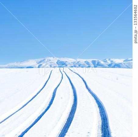 青空と圧雪道路に車が通った跡がある冬の北海道美瑛町の丘の道 133564682