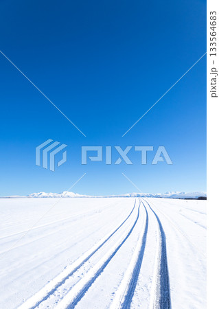 青空と圧雪道路に車が通った跡がある冬の北海道美瑛町の丘の道 133564683