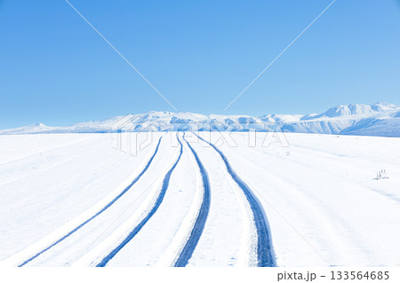青空と圧雪道路に車が通った跡がある冬の北海道美瑛町の丘の道 133564685