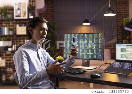 Self employed man speaking with business partner during online meeting. Asian male entrepreneur manages company tasks, sharing marketing strategy plans with colleagues through cellphone video call. 133565730