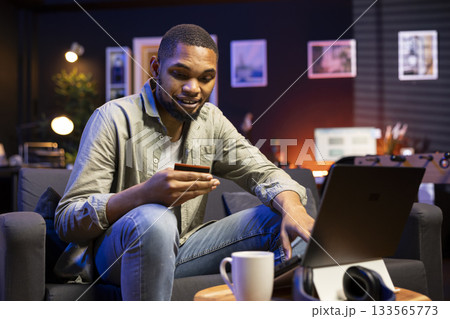 Casual young man at home entering card digits to renew an account subscription, managing the services on laptop. Person transferring money on the internet, updating the credentials. 133565773