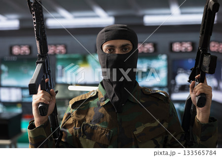 Portrait of dangerous masked terrorist holding assault rifles able to engage targets at extended range with accurate, lethal fire. Insurgent using guns, assaulting enemy base during guerilla war 133565784