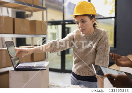 Staff members ensuring accurate order processing on a laptop, checking stock inventory in a small scale depot. Supporting e-business services with retail shipment and in house quality control. 133565858