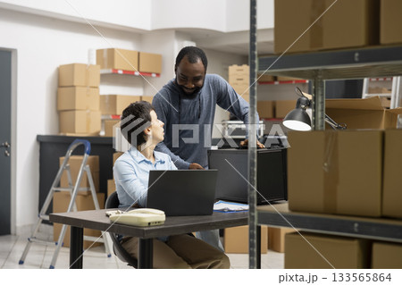 Multiethnic staff collaborates in order processing storage room, surrounded by packages and technology systems in a modern inventory depot designed for small scale distribution services. Multiethnic staff collaborates in order processing storage room, surrounded by packages and technology systems in a modern inventory depot designed for small scale distribution services. 133565864