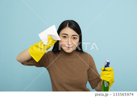 Happy asian woman in yellow rubber gloves holding cleaning products and looking at camera. Young female housekeeper stands on isolated background, prepared for household morning chores. 133565974