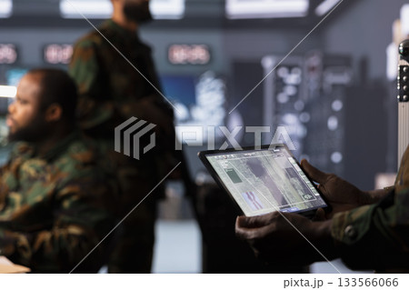 Military operator monitoring enemy aerial attacks using digital device. Army soldier in headquarters maintains air space superiority with radar on tablet during armed conflict, close up 133566066