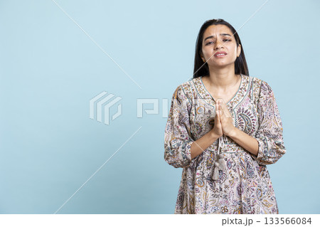 Indian girl holding hands together in a prayer or begging symbol, showing spiritual meditation and hoping for something better in the studio. Faithful devoted girl with belief and faith. Indian girl holding hands together in a prayer or begging symbol, showing spiritual meditation and hoping for something better in the studio. Faithful devoted girl with belief and faith. 133566084