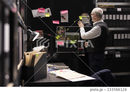 Police commissioner studying important details and clues on mystery board in incident room, arranging case files and evaluating proof for a criminal investigation. Connecting the dots. Police commissioner studying important details and clues on mystery board in incident room, arranging case files and evaluating proof for a criminal investigation. Connecting the dots. 133566128