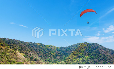Outdoor scene featuring a paraglider soaring through a clear blue sky over lush green hills. Natural background 133568022