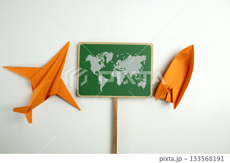 Orange paper airplane and boat with a signboard of a worldwide map on a white background. Concept of travel, exploration, and navigation Orange paper airplane and boat with a signboard of a worldwide map on a white background. Concept of travel, exploration, and navigation 133568191