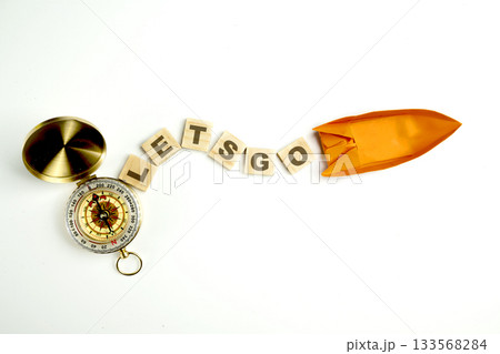 Orange paper boat with antique compass and wooden cubes with let's go text isolated over a white background. Concept of travel, exploration, and navigation 133568284