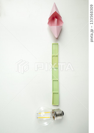 Top view of a lightbulb with rectangular blocks and a paper sailboat on a white background. Concept of travel, exploration, and navigation 133568309