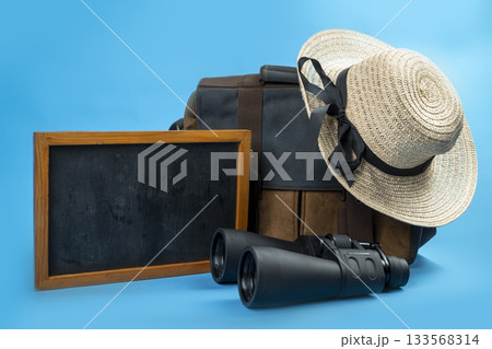 Chalkboard and Canvas bag with binoculars and a straw hat with a black ribbon on a blue background. Mockup or Copy space. Concept of travel, summer, or vacation 133568314