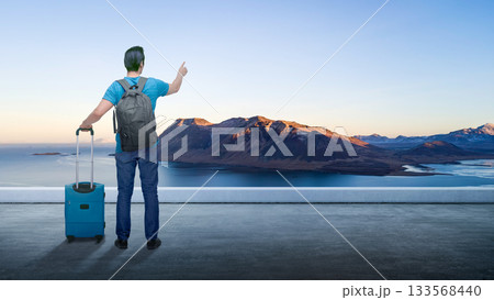 Indonesian southeast asian man with a backpack carrying a suitcase standing and looking out view of the mountain landscape. Concept of travel Indonesian southeast asian man with a backpack carrying a suitcase standing and looking out view of the mountain landscape. Concept of travel 133568440