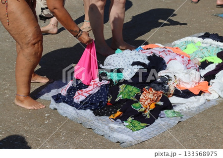 Street vendor arranging colorful clothes on beach towel at outdoor market 133568975