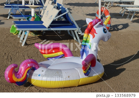 Inflatable unicorn float resting on sandy beach near lounge chairs 133568979