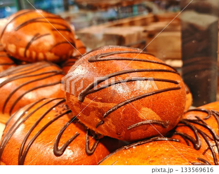Fresh Sweet Buns with Chocolate Drizzle. Close-up of appetizing golden-brown sweet buns topped with glossy chocolate icing stripes. Perfect bakery display, dessert and pastry concept 133569616