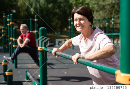 Mature woman doing push-ups from the crossbar on outdoor sports ground 133569736