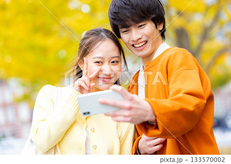 銀杏の前で自撮りをするカップル 133570002