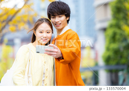 銀杏の前で自撮りをするカップル 133570004