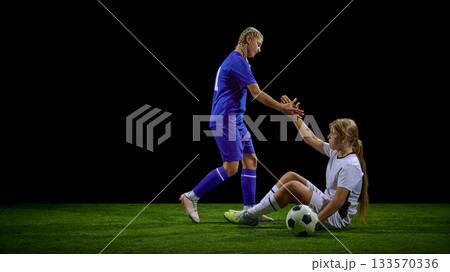 Teenage female soccer player offering hand to help opponent stand up Teenage female soccer player offering hand to help opponent stand up 133570336