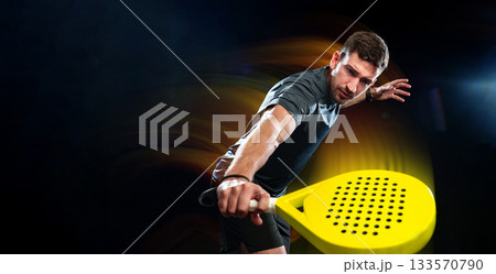 Man playing paddle tennis in a dark indoor court with colorful lights at night 133570790