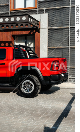 Bright red pickup truck parked in front of a modern building in the afternoon sun 133570856